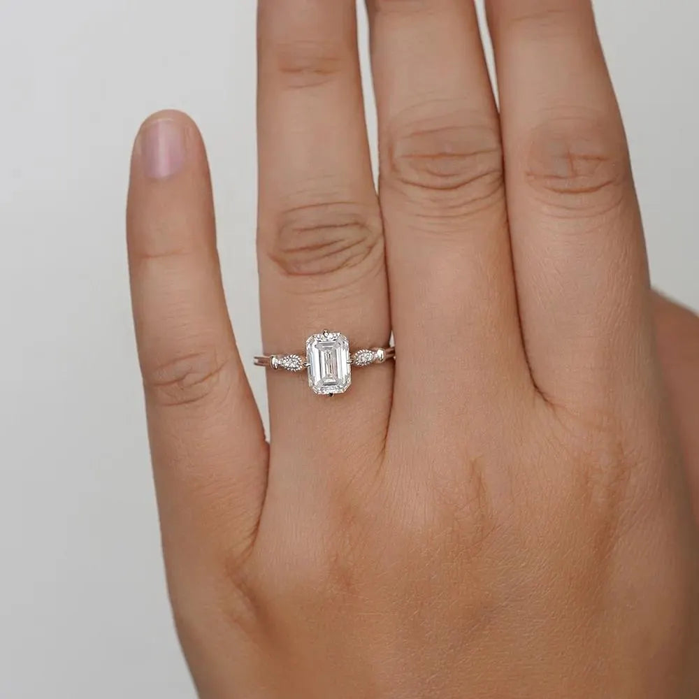 Elegant Emerald Cut Solitaire Engagement Ring In White Gold With Dainty Accent Stones. A Timeless Moissanite Wedding Or Promise Ring For Her